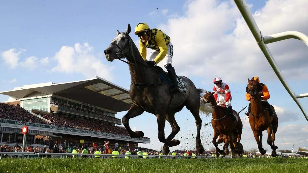 Caballo y jockey cruzando la línea de meta victoriosos en el Grand National de Aintree